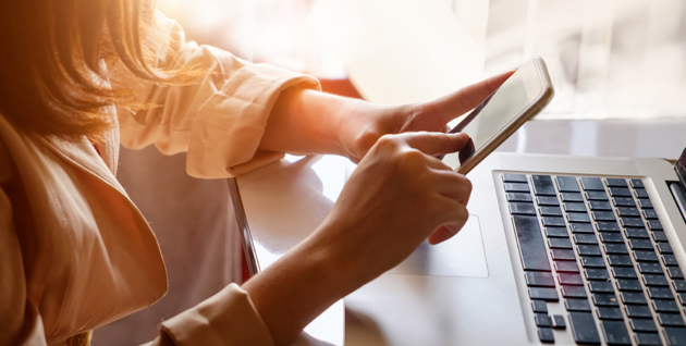 Woman looking at phone next to her laptop